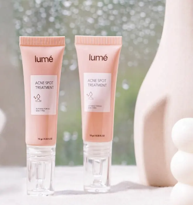 Dua tube Acne Spot Treatment dan vas putih di depan jendela berembun