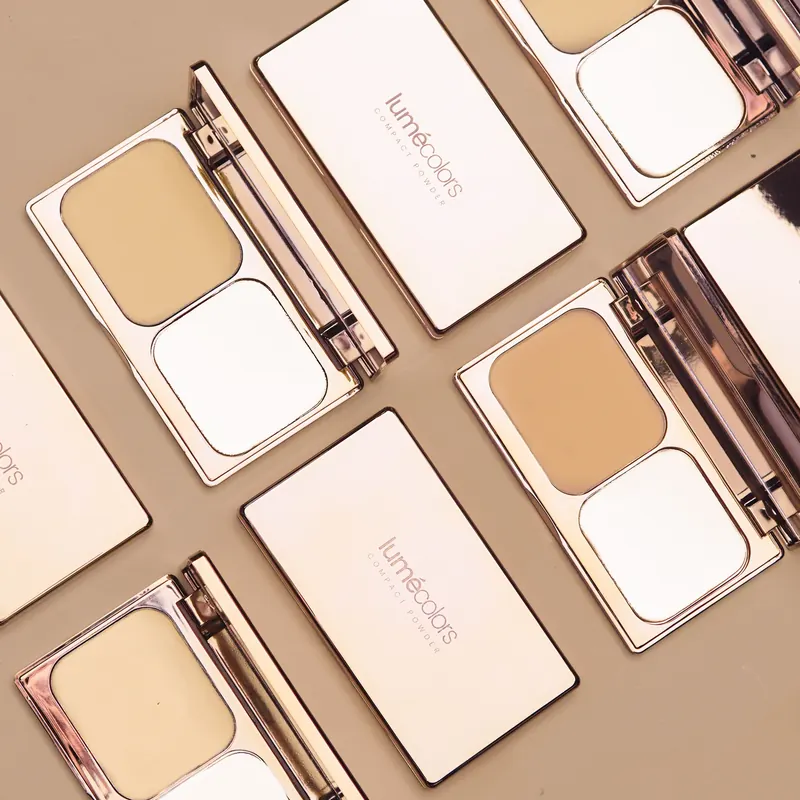 Beberapa Lumécolors Compact Powder berbingkai rose-gold, terbuka dan tertutup, di atas latar taupe