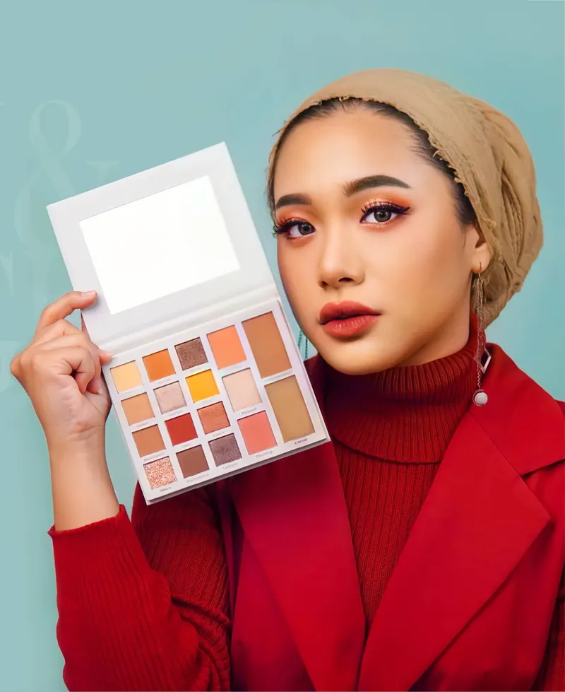 Model berhijab krem dan mantel merah memegang Day & Night Palette yang terbuka di samping wajahnya