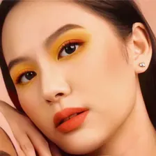 Model berambut gelap dengan eyeshadow kuning dan bibir oranye