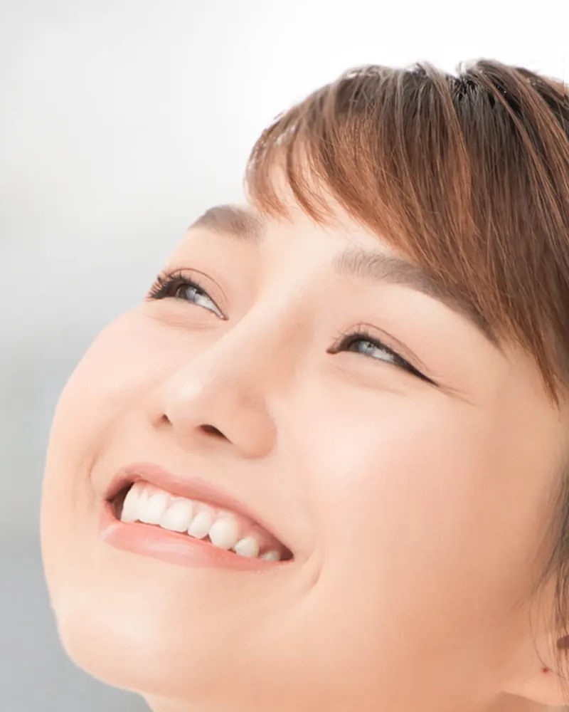 Perempuan tersenyum menengadahkan wajah ke semprotan face mist