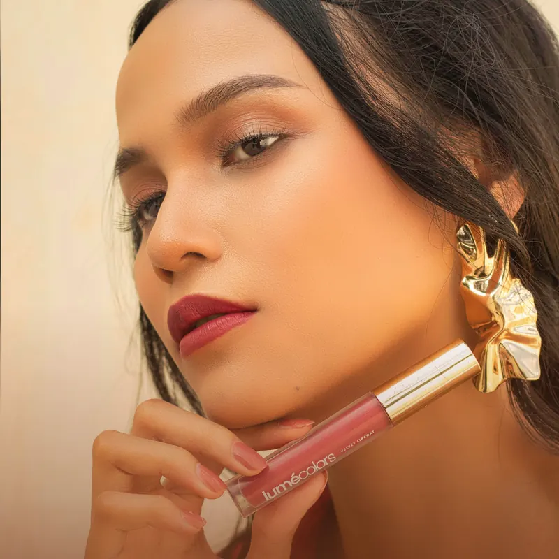 Model beranting emas memegang Lumécolors Velvet Lipcoat di dagunya, bibir merah matte