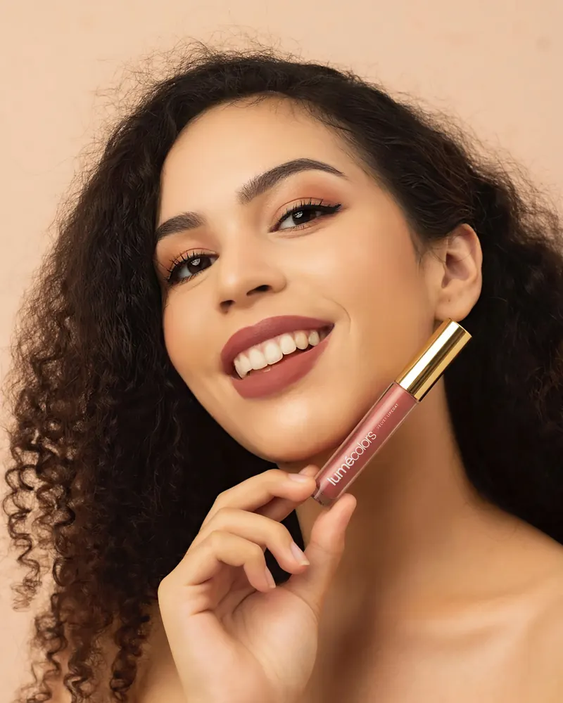 Model berambut ikal tersenyum sambil memegang Lumécolors Velvet Lipcoat di rahangnya