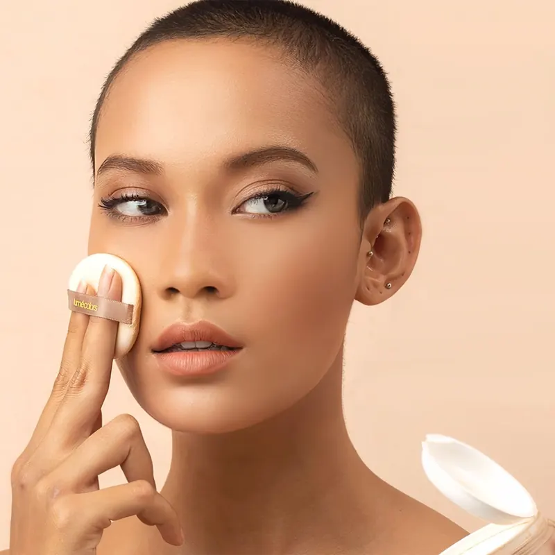 Model berambut cepak menepuk puff Lumécolors ke pipinya, jar Loose Powder terbuka di sudut bawah
