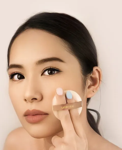 Model berambut hitam diikat menepuk puff Lumécolors ke pipinya